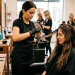 Professional expert salon stylist applying premium liquid smoothing treatment to a female clients long beautiful brown hair. (1)